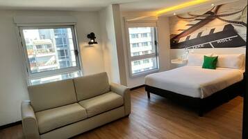 A modern hotel room with a bed, a sofa, and two windows.