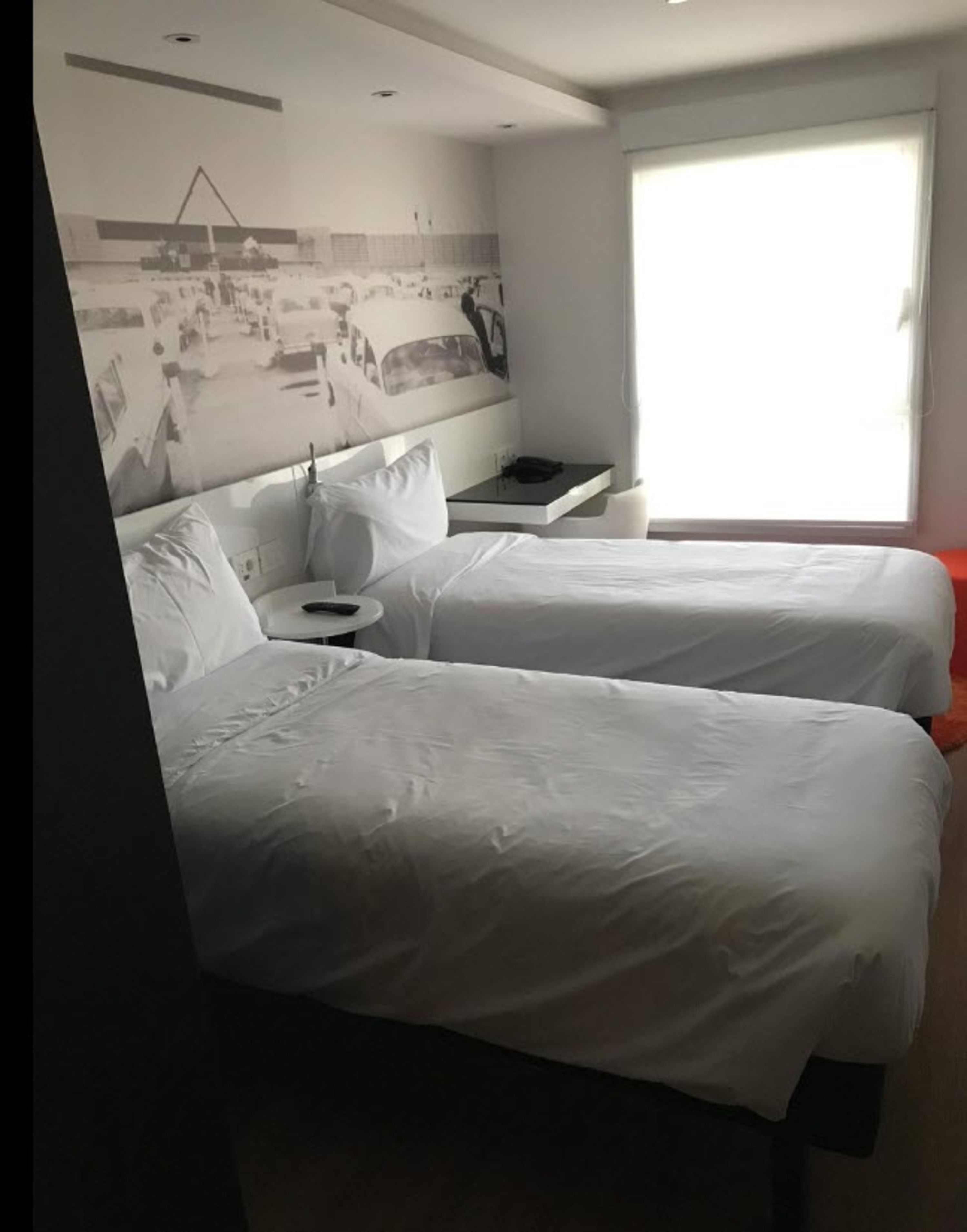 A hotel room with two beds, a small table, a chair, and a window with a view of a building.