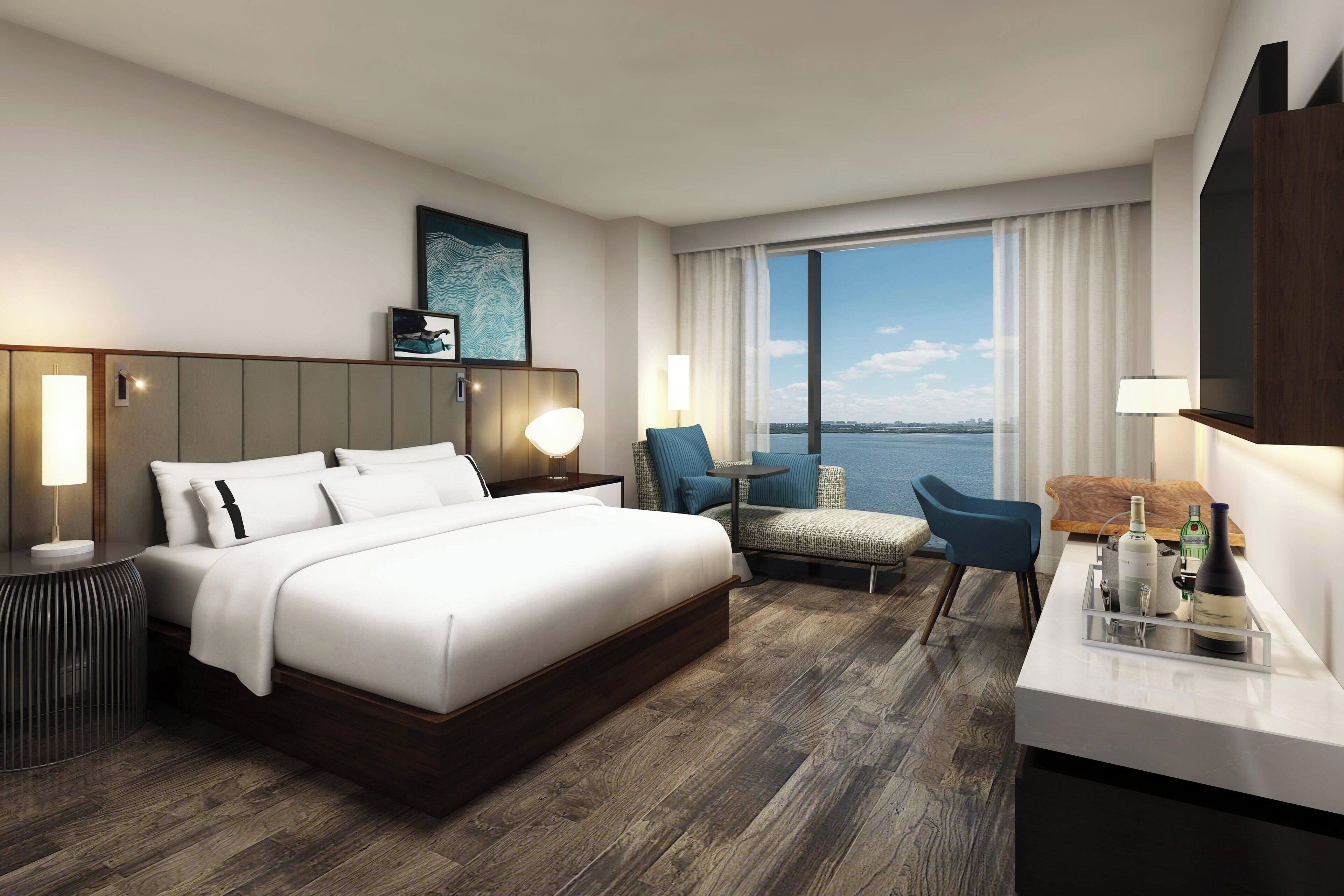 A modern hotel room with a large bed, a seating area with a view, and a desk with amenities.