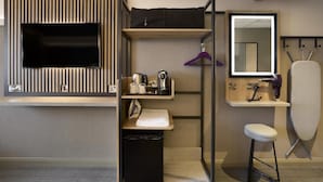 A compact hotel room with a flat-screen TV, a small kitchenette, a mirror, and a foldable ironing board. - Premier Inn London Hayes Heathrow - Hyde Park (Hayes)