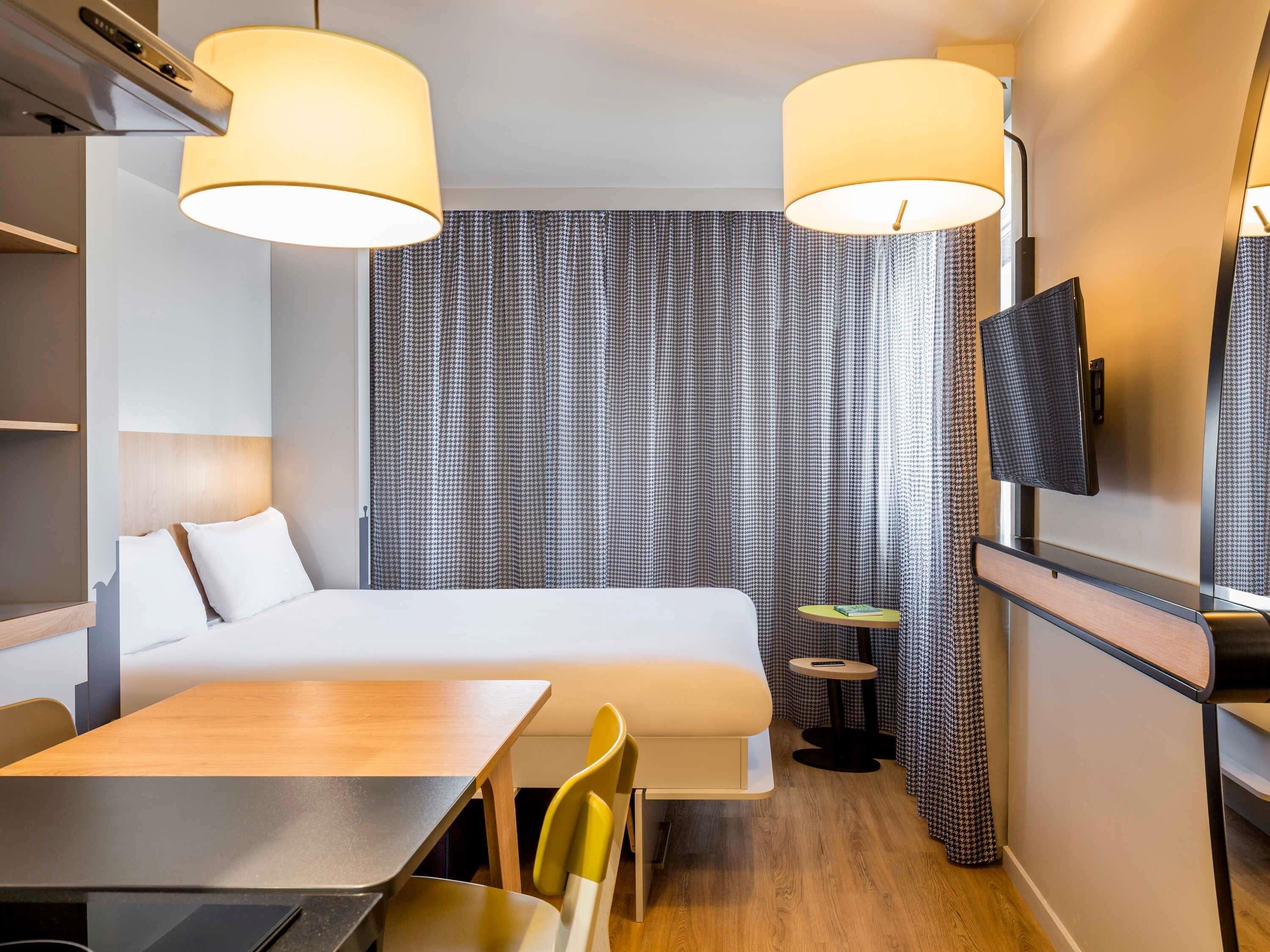 Een hotelkamer met een bed, een bureau, twee stoelen, een klein tafeltje, een televisie en een tv aan de muur.