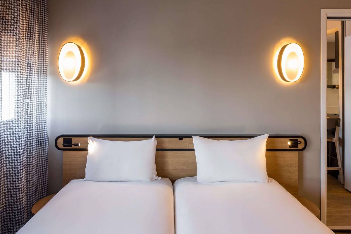 Uma cama de casal com duas almofadas, cabeceira de madeira e duas luminárias fixadas na parede.