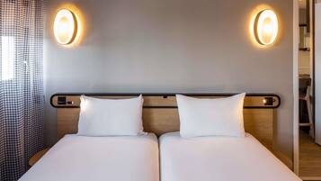 A double bed with two pillows, a wooden headboard, and two wall-mounted light fixtures.