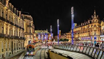 Eine beleuchtete Straße mit einer Straßenbahn, historischen Gebäuden und einer gebogenen Brücke.