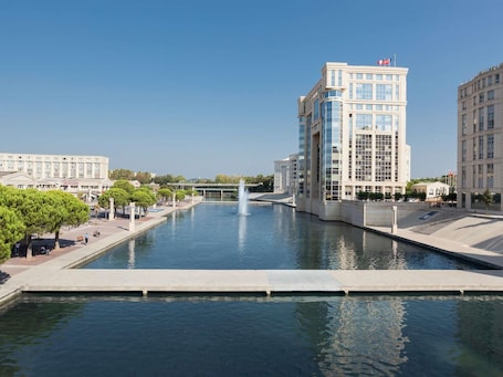 A modern building with a reflective glass facade, a water feature in the foreground, and a clear sky.. Aparthotel Adagio Access Montpellier Centre