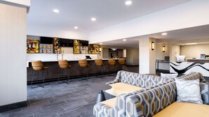 Un moderno vestíbulo de hotel con zona de bar, asientos y una mesa de recepción.