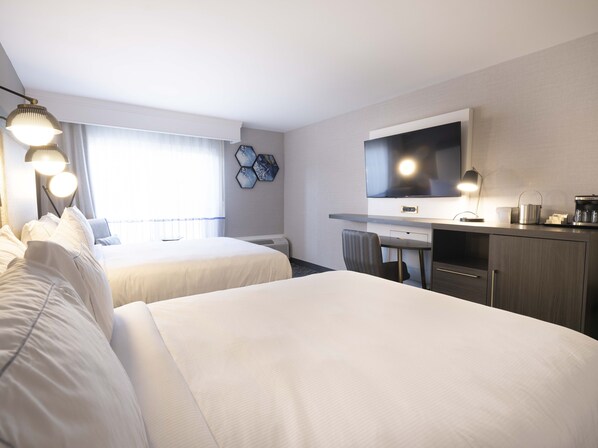 Habitación de hotel con dos camas, un escritorio, un televisor de pantalla plana, cafetera y calefacción en la pared.