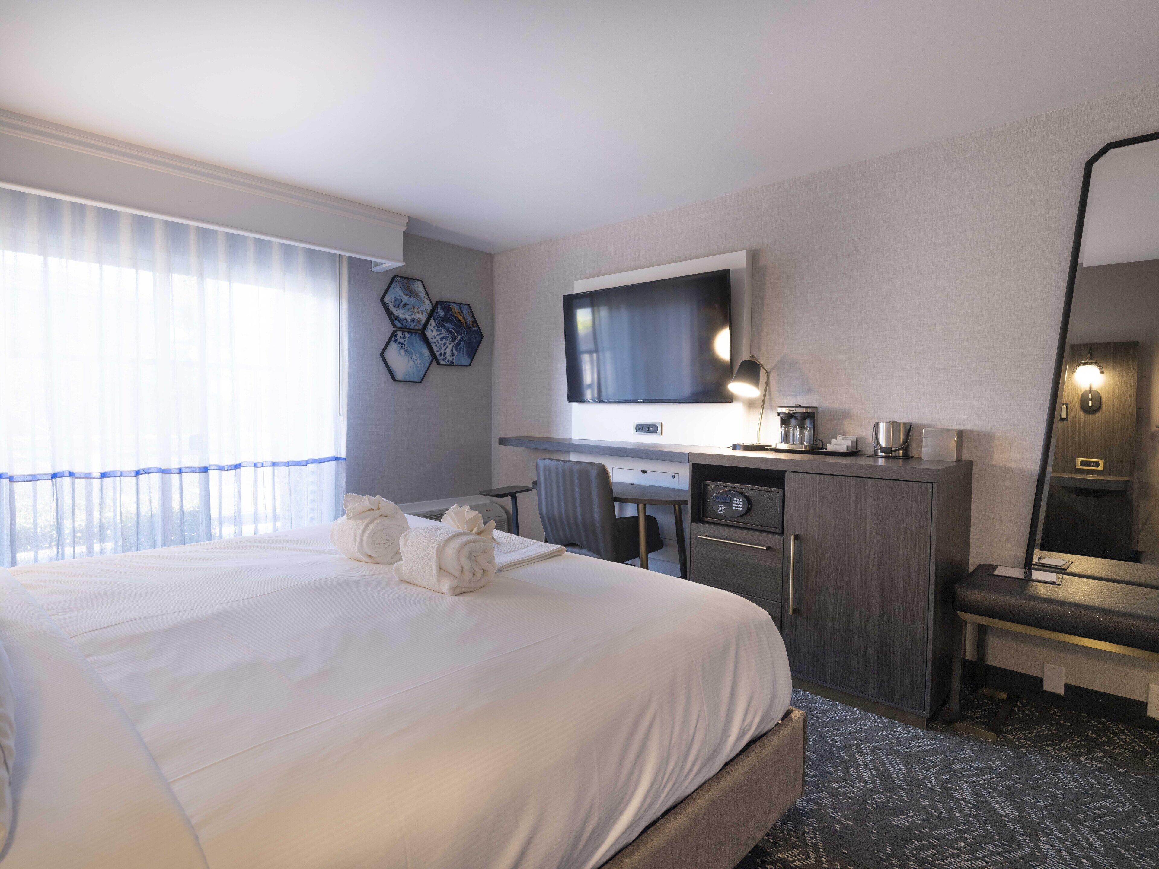 Ein Hotelzimmer mit einem großen Bett, einem Schreibtisch, einem Stuhl, einem Fernseher und einem Spiegel.