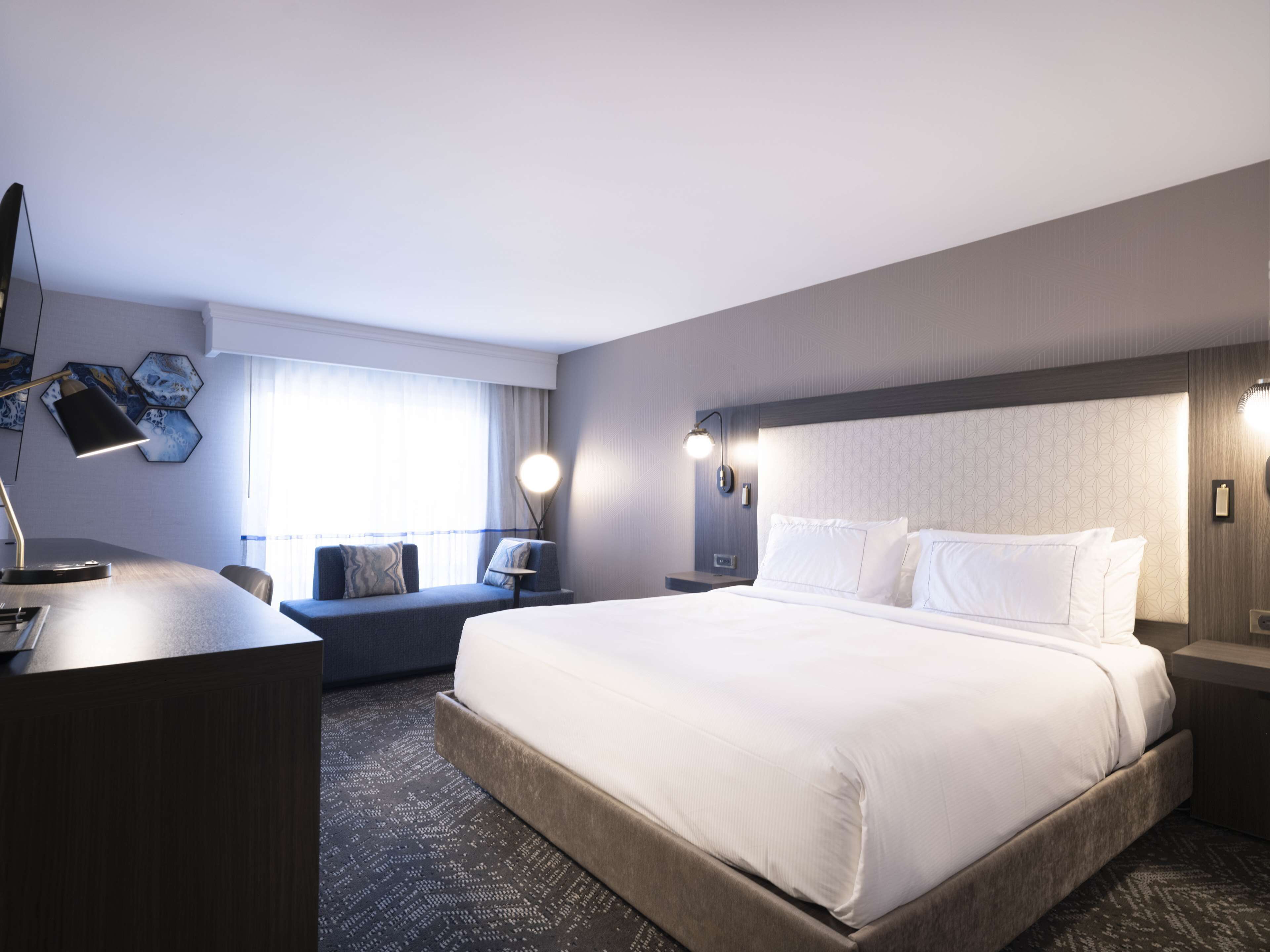Ein modernes Hotelzimmer mit einem großen Bett, einem Schreibtisch und einer Sitzecke am Fenster.