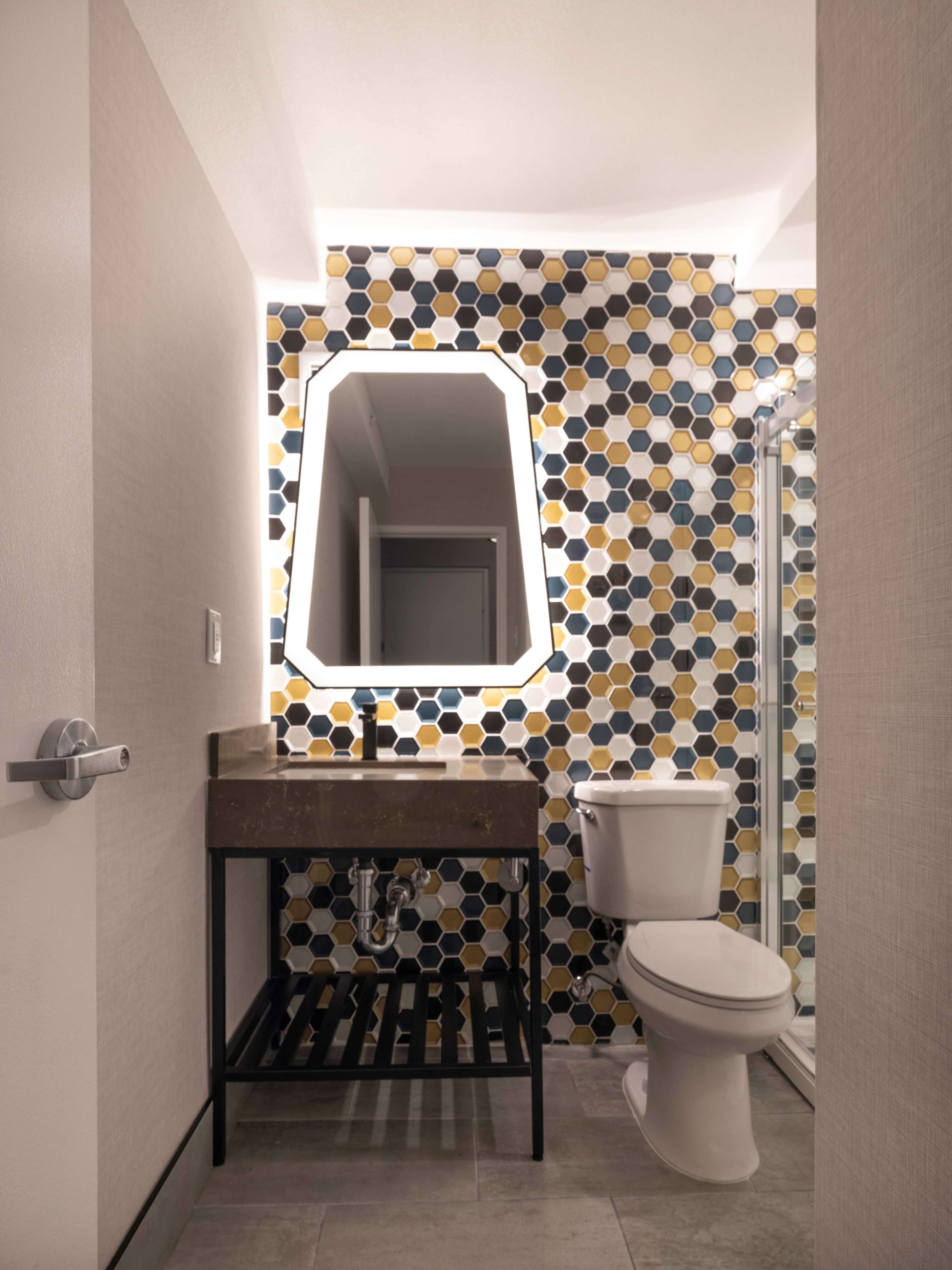 A modern bathroom with a hexagonal tile backsplash, a rectangular mirror, a sink with a black metal frame, and a toilet.