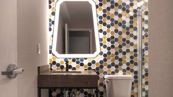 A modern bathroom with a hexagonal tile backsplash, a rectangular mirror, a sink with a black metal frame, and a toilet.
