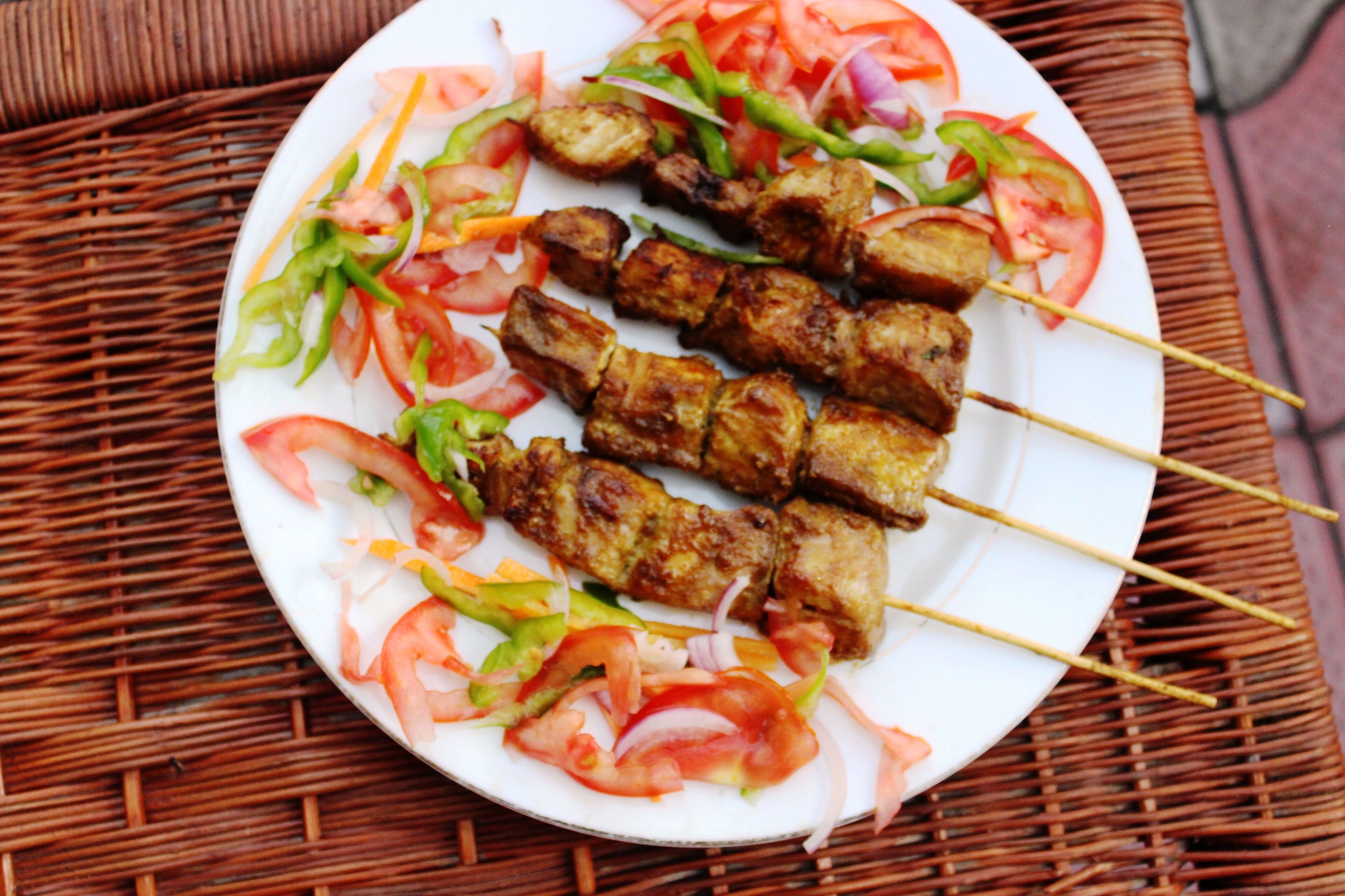 A plate of skewered meat with vegetables on a white plate.
