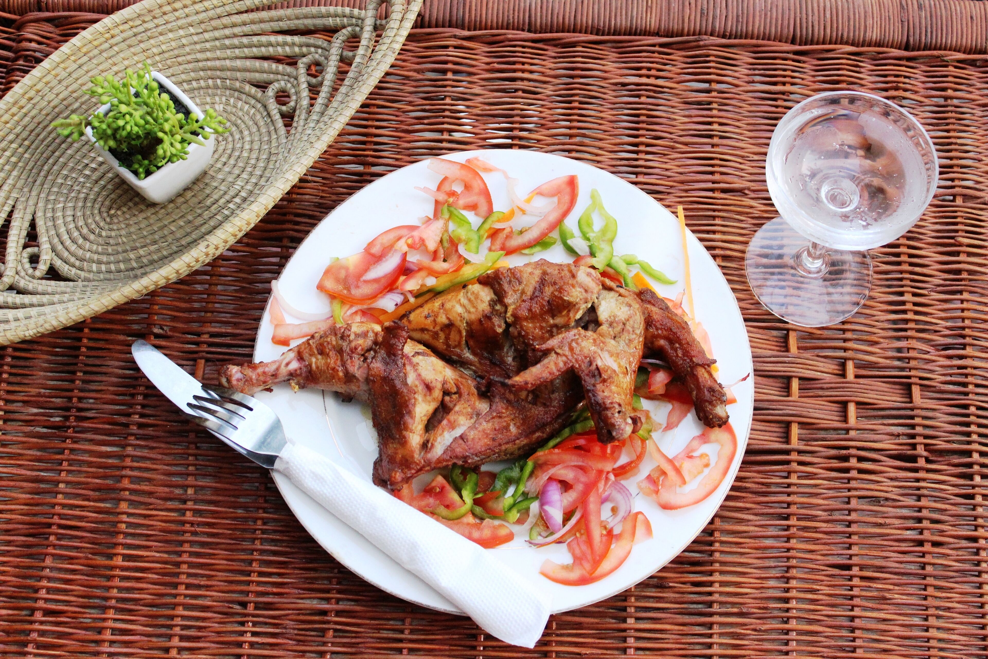 A plate of grilled chicken with vegetables on a wicker table.
