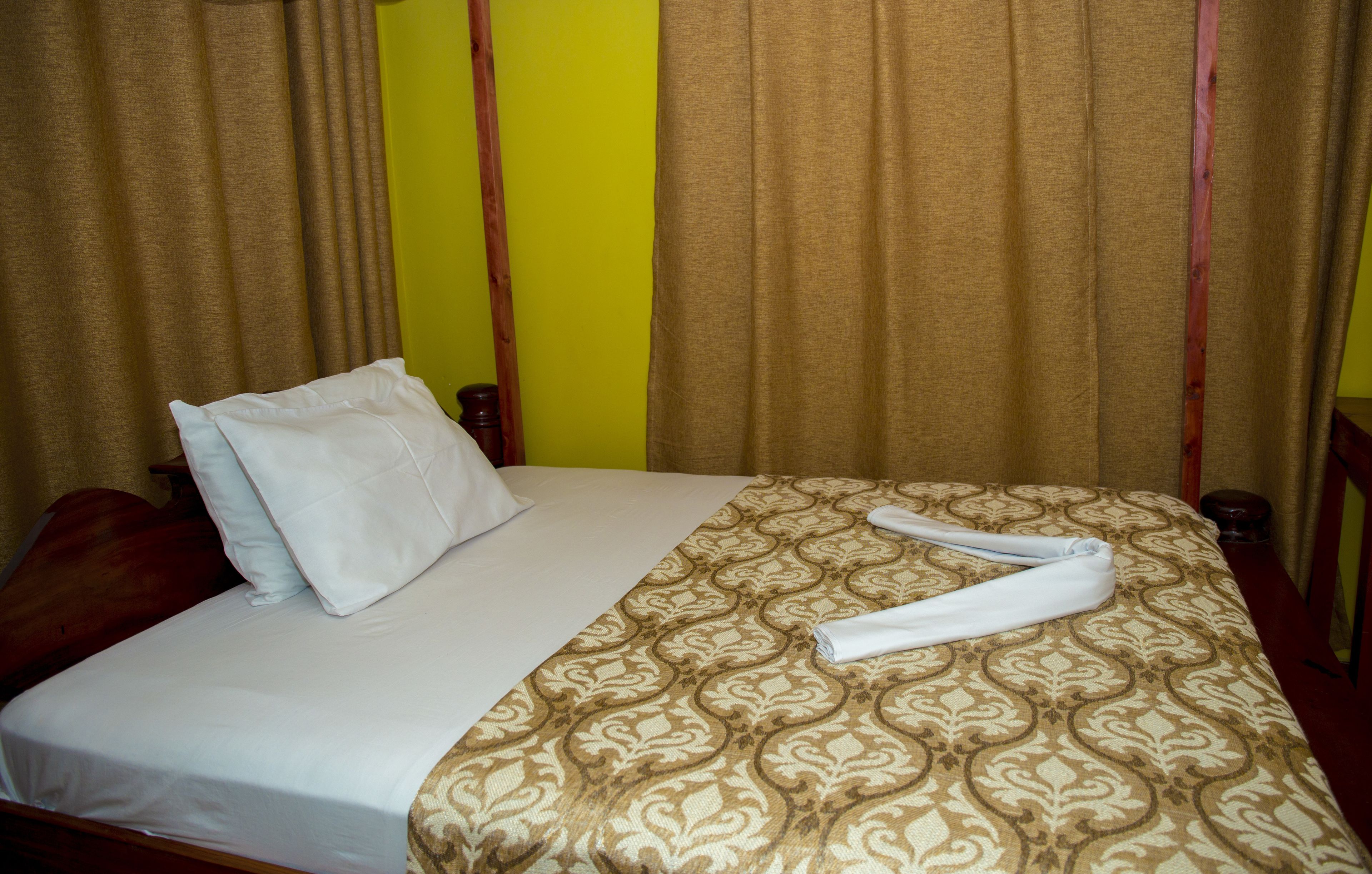 Une chambre d’hôtel avec un lit, des oreillers, une serviette pliée et des rideaux.