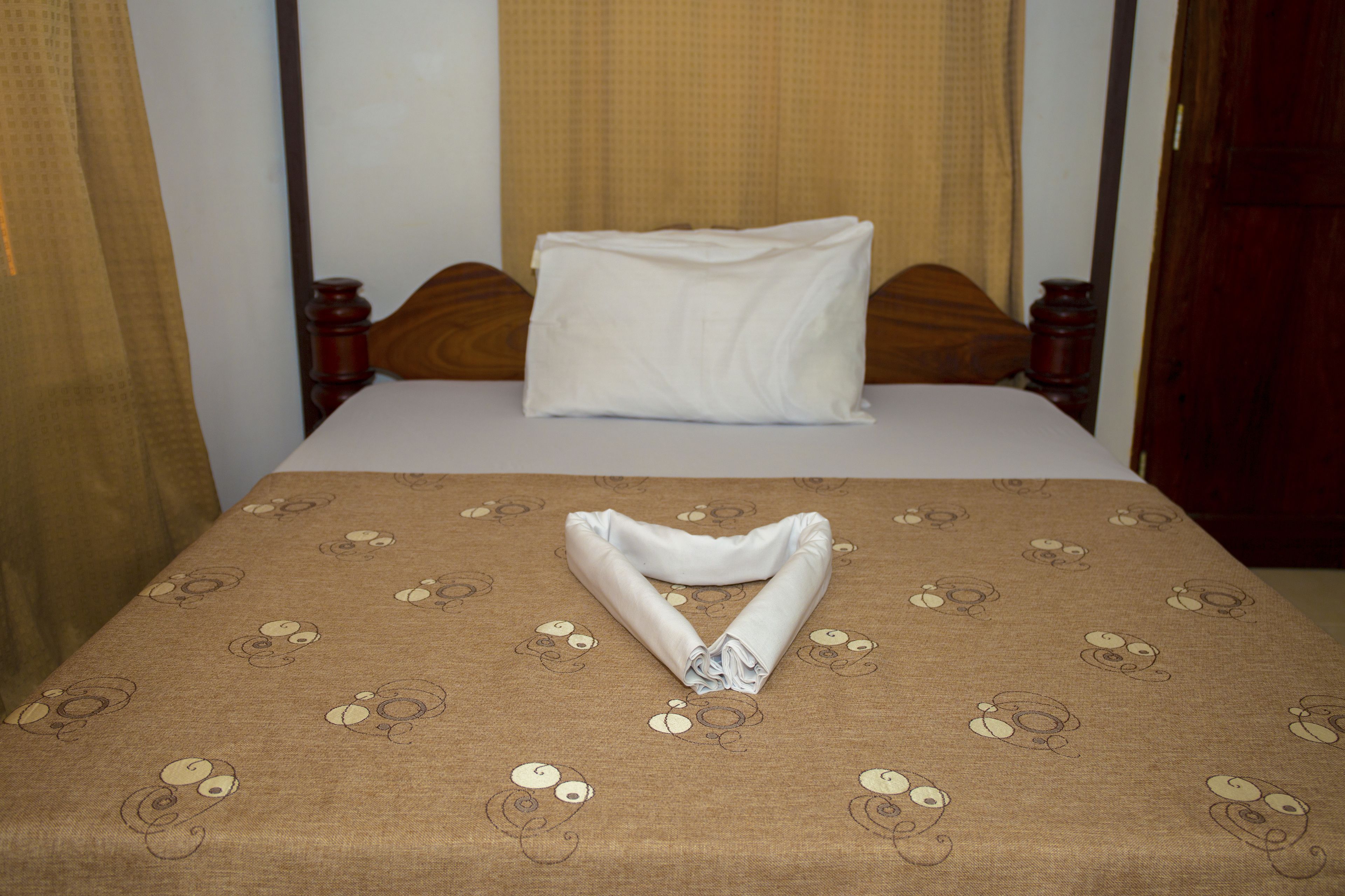 Una cama bien hecha con una colcha marrón estampada y una toalla blanca doblada.