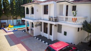 Une maison à deux étages avec un balcon, une piscine et une voiture rouge garée devant.