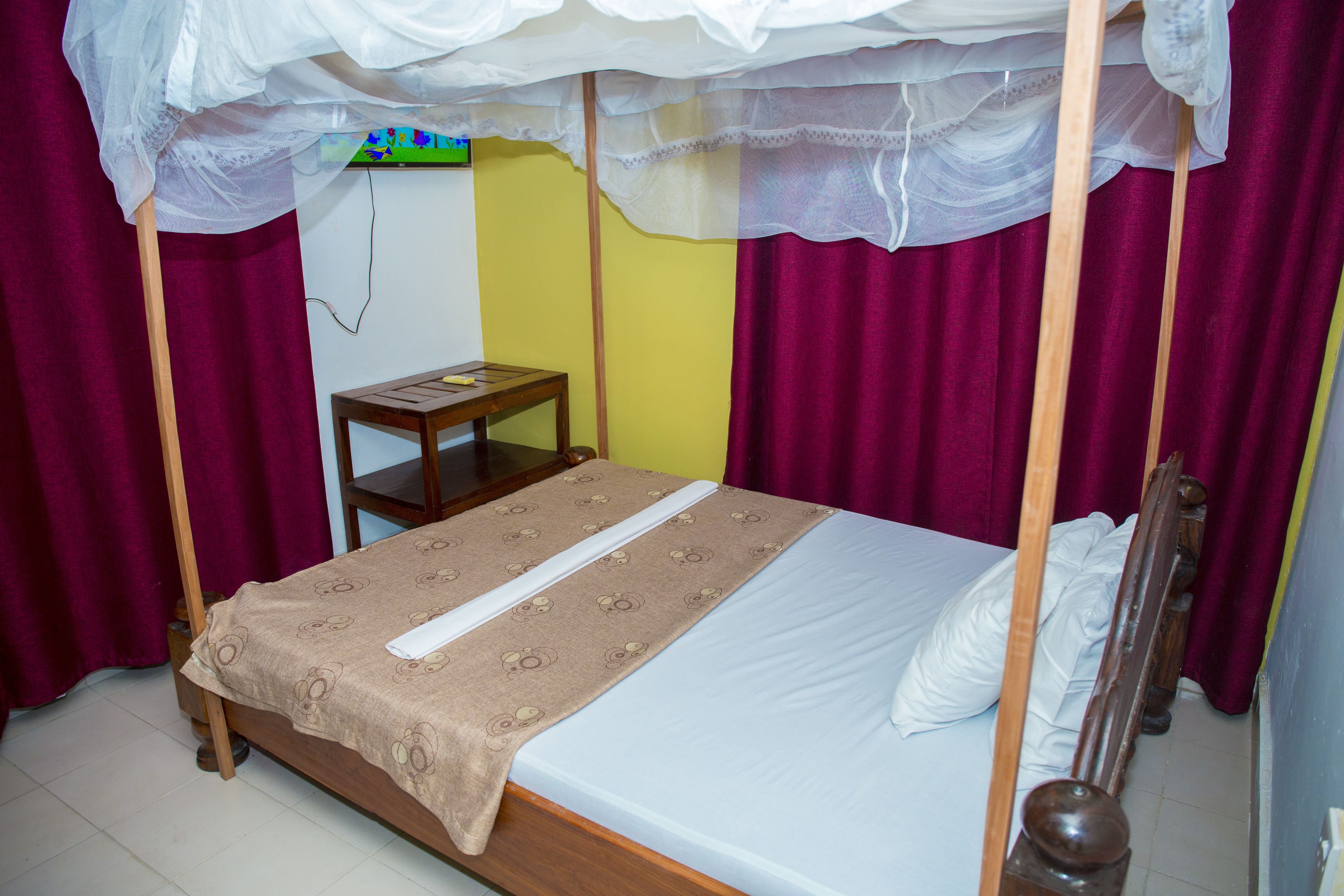 Una cama individual con dosel, una mesita de noche de madera y un televisor instalado en la pared.