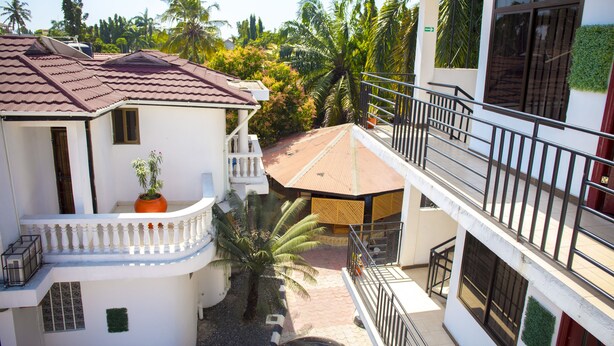 Un immeuble à plusieurs étages doté de balcons, d’un toit en tuiles et entouré d’une végétation tropicale.