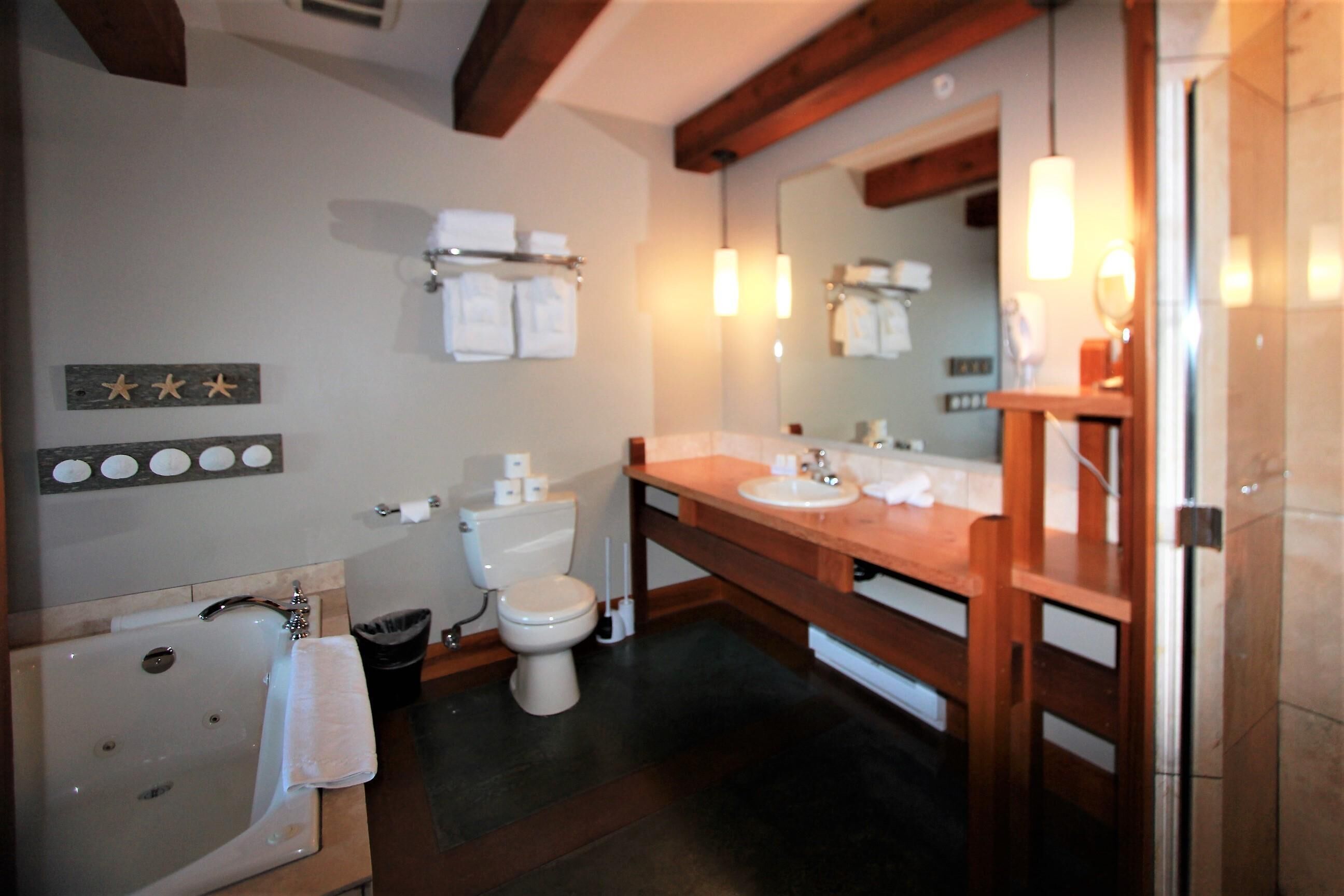 A bathroom with a bathtub, toilet, and sink. There are towels hanging on a rack, a mirror above the sink, and a wooden shelf with toiletries.