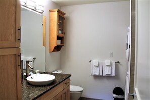 A bathroom with a wooden cabinet, a sink, a toilet, and a towel rack. - Marina View (Ucluelet)
