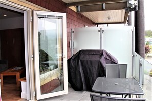 An open sliding glass door leading to a covered patio area with a table and chairs. - Marina View (Ucluelet)