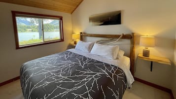 Een slaapkamer met een groot bed, een raam met uitzicht op een meer en een houten plafond.