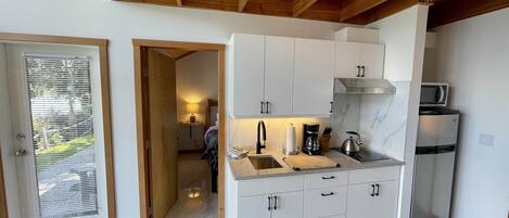 A modern kitchen with white cabinets, a stainless steel refrigerator, a microwave, and a wooden ceiling.