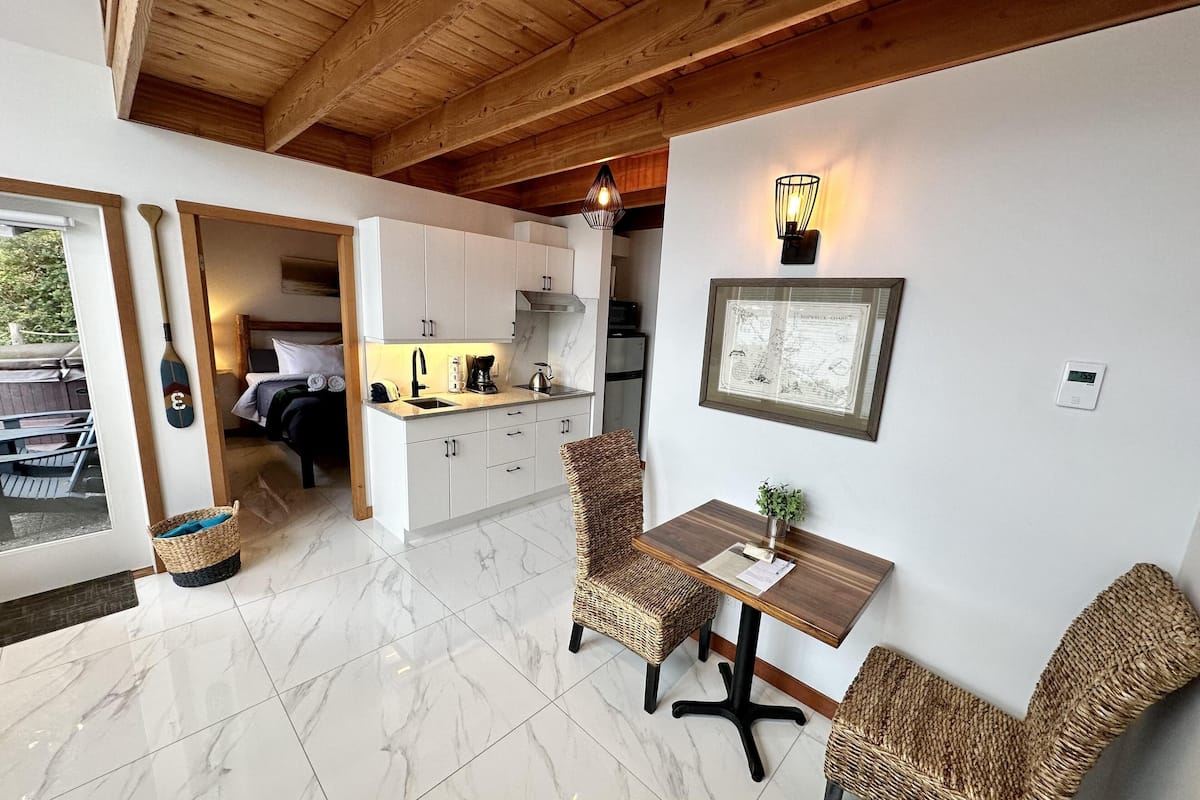 Une cuisine moderne avec des meubles blancs, un coin repas doté de chaises en osier et un plafond en bois.