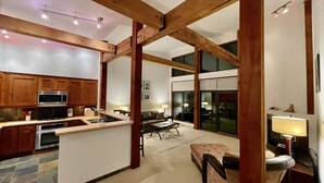 A spacious kitchen with wooden beams, a dining area with a table and chairs, and a view through large sliding glass doors. - Big Beach Villa (Ucluelet)