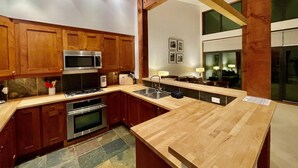 A modern kitchen with wooden cabinets, stainless steel appliances, and a large island with a sink. - Big Beach Villa (Ucluelet)
