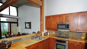 A modern kitchen with wooden cabinets, a built-in microwave, a stove, and a sink. - Pacific Rim Retreat (Ucluelet)