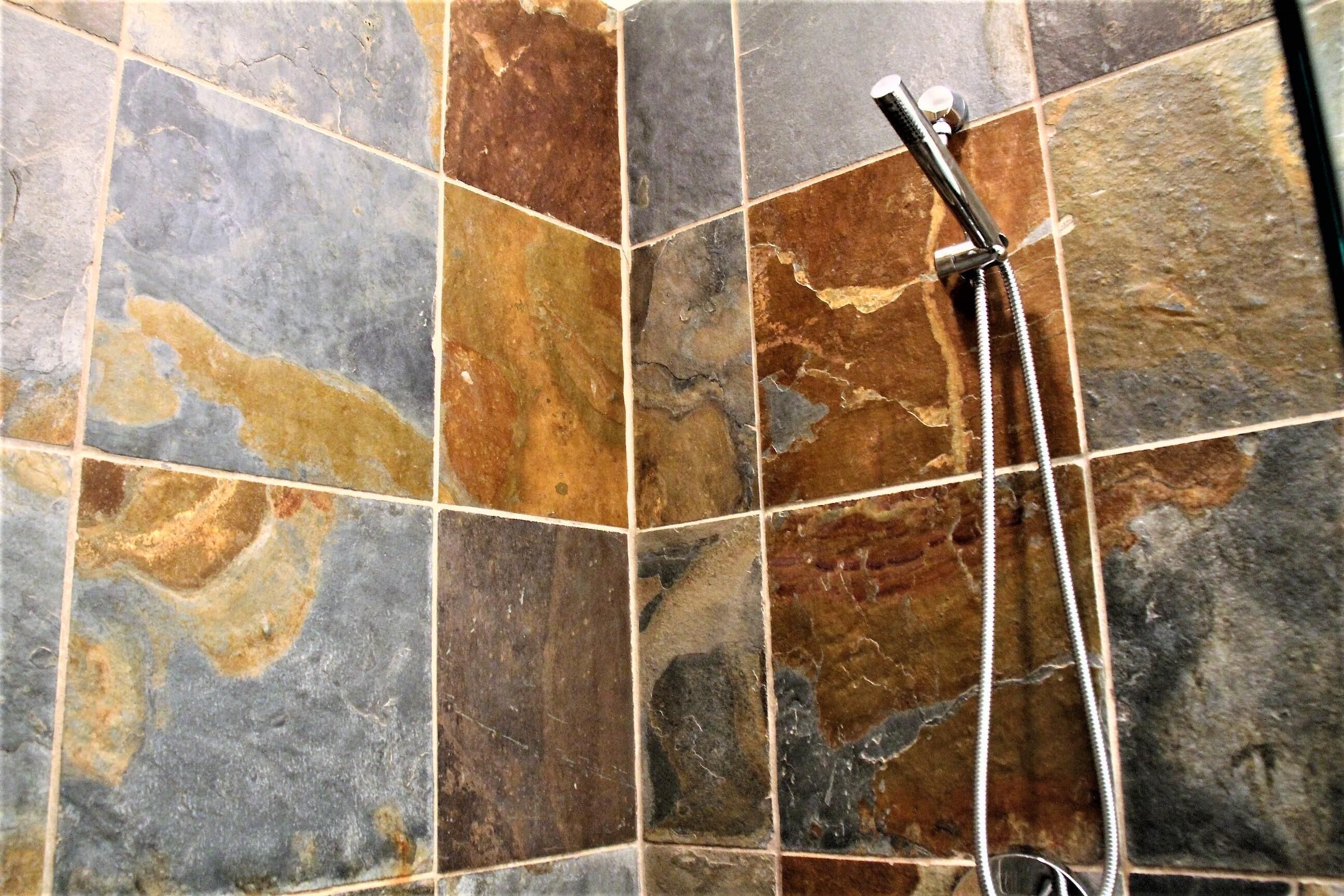 A shower area with a handheld showerhead and a wall-mounted faucet.