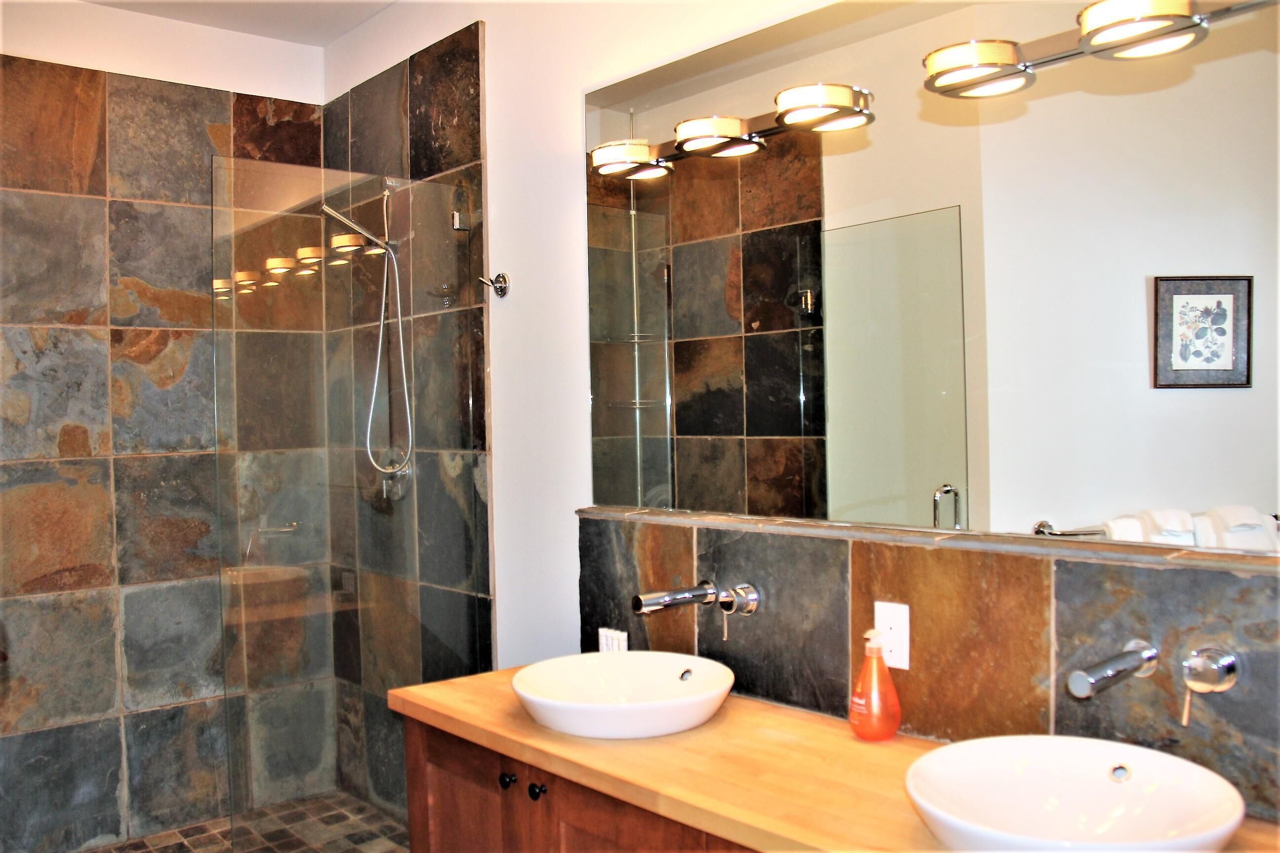 A bathroom with a glass-enclosed shower, two sinks, and a large mirror with lights.