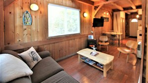 Una habitación acogedora con paredes de madera, un sofá con cojines, una mesa de centro de madera y un televisor.
