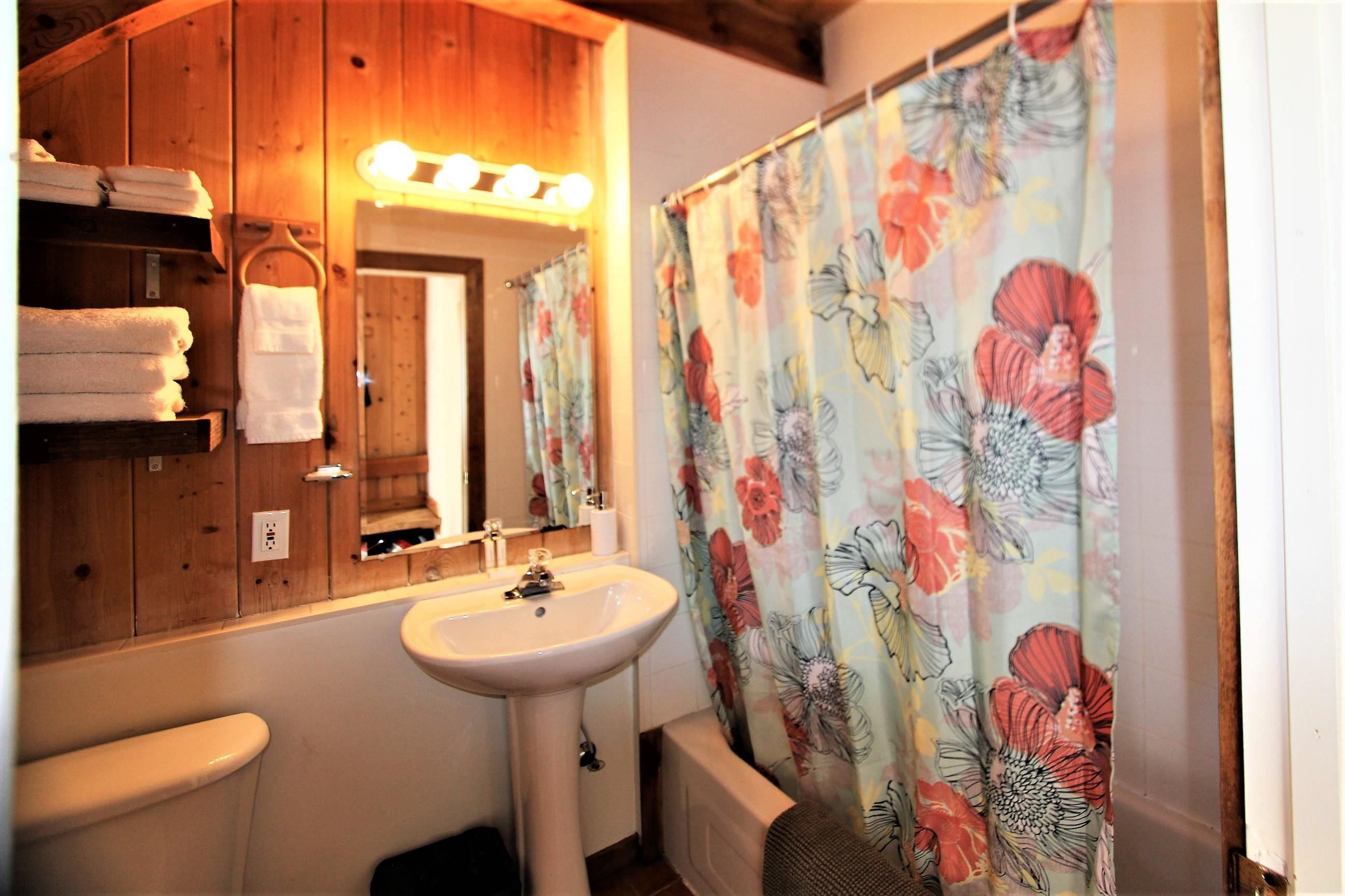A bathroom with a wooden vanity, a sink, and a shower curtain with floral patterns.