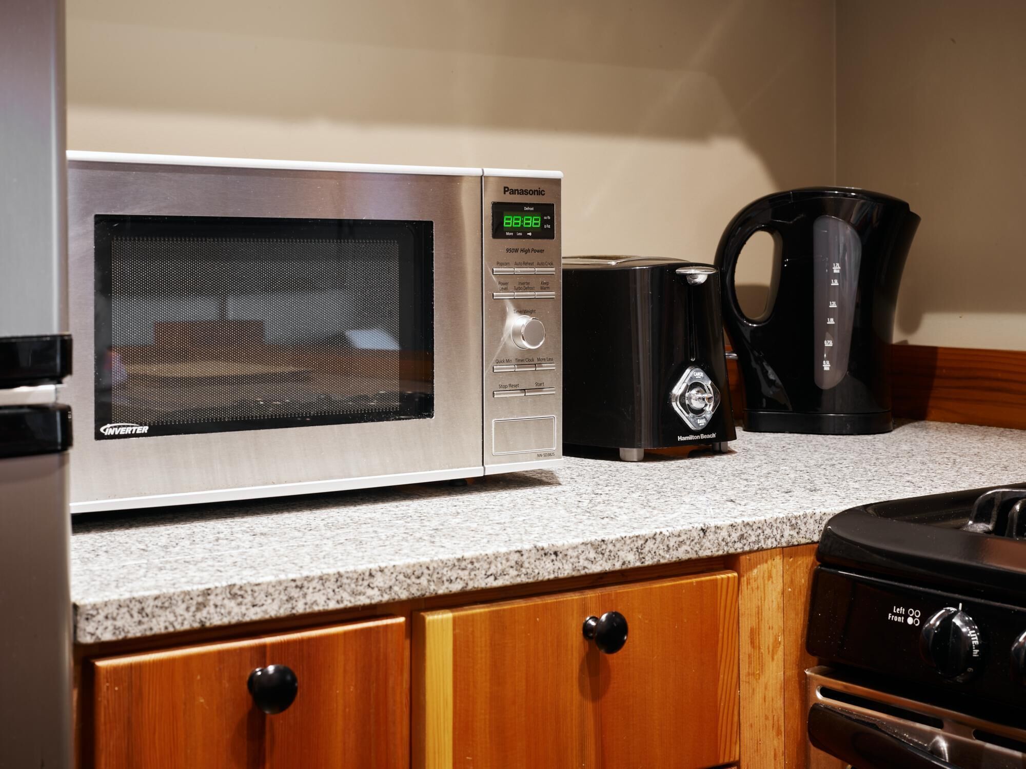Una cocina con un microondas de acero inoxidable, una cafetera Hamilton Beach y una estufa.