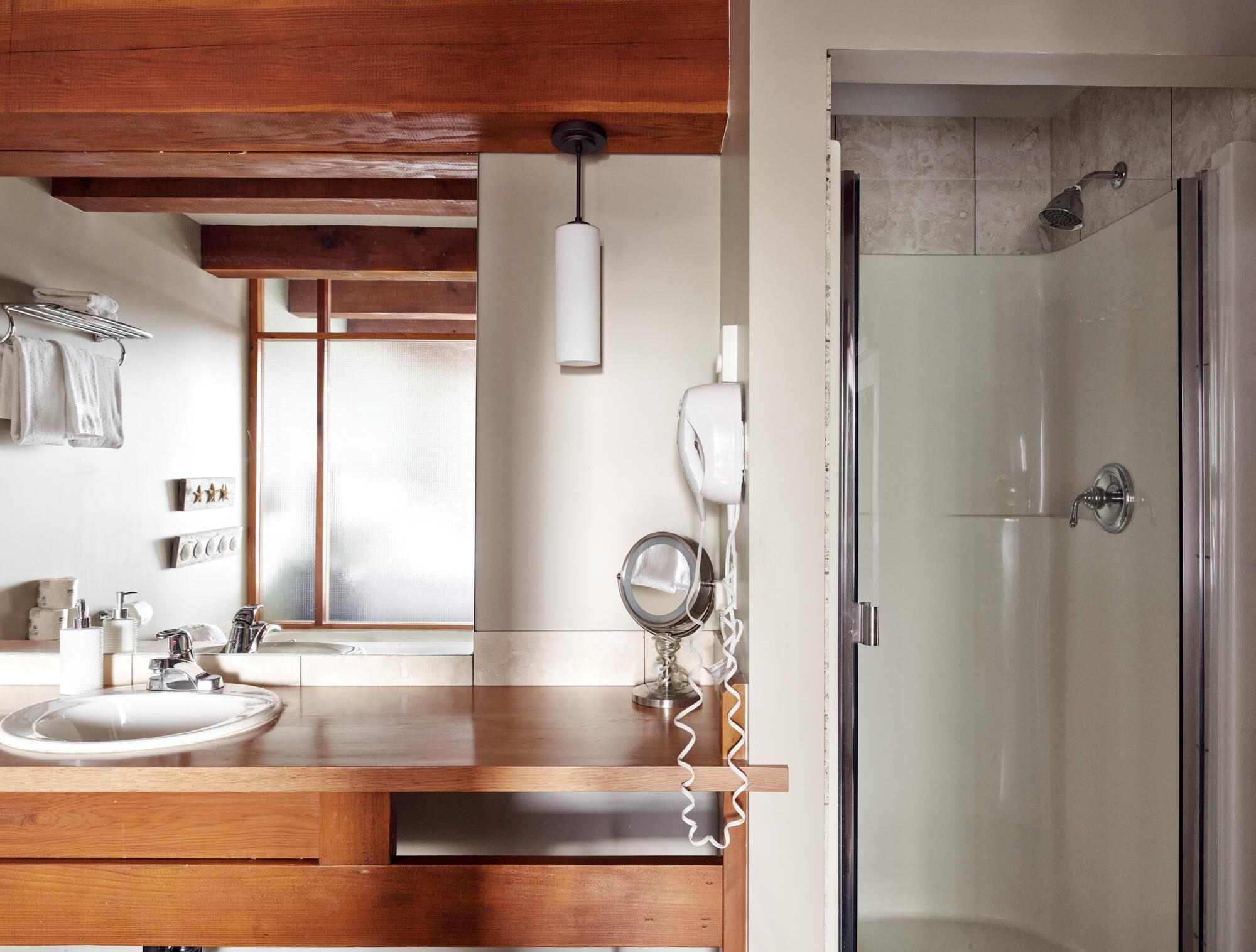A bathroom with a wooden vanity, a sink, a mirror, a hairdryer, and a shower.