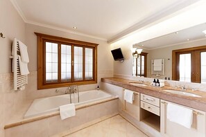A bathroom with a bathtub, two sinks, a large mirror, and a window with wooden frames.