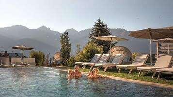 A swimming pool with lounge chairs and umbrellas, surrounded by trees and mountains in the background.