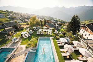A resort with a swimming pool, lounge chairs, and a mountainous backdrop.