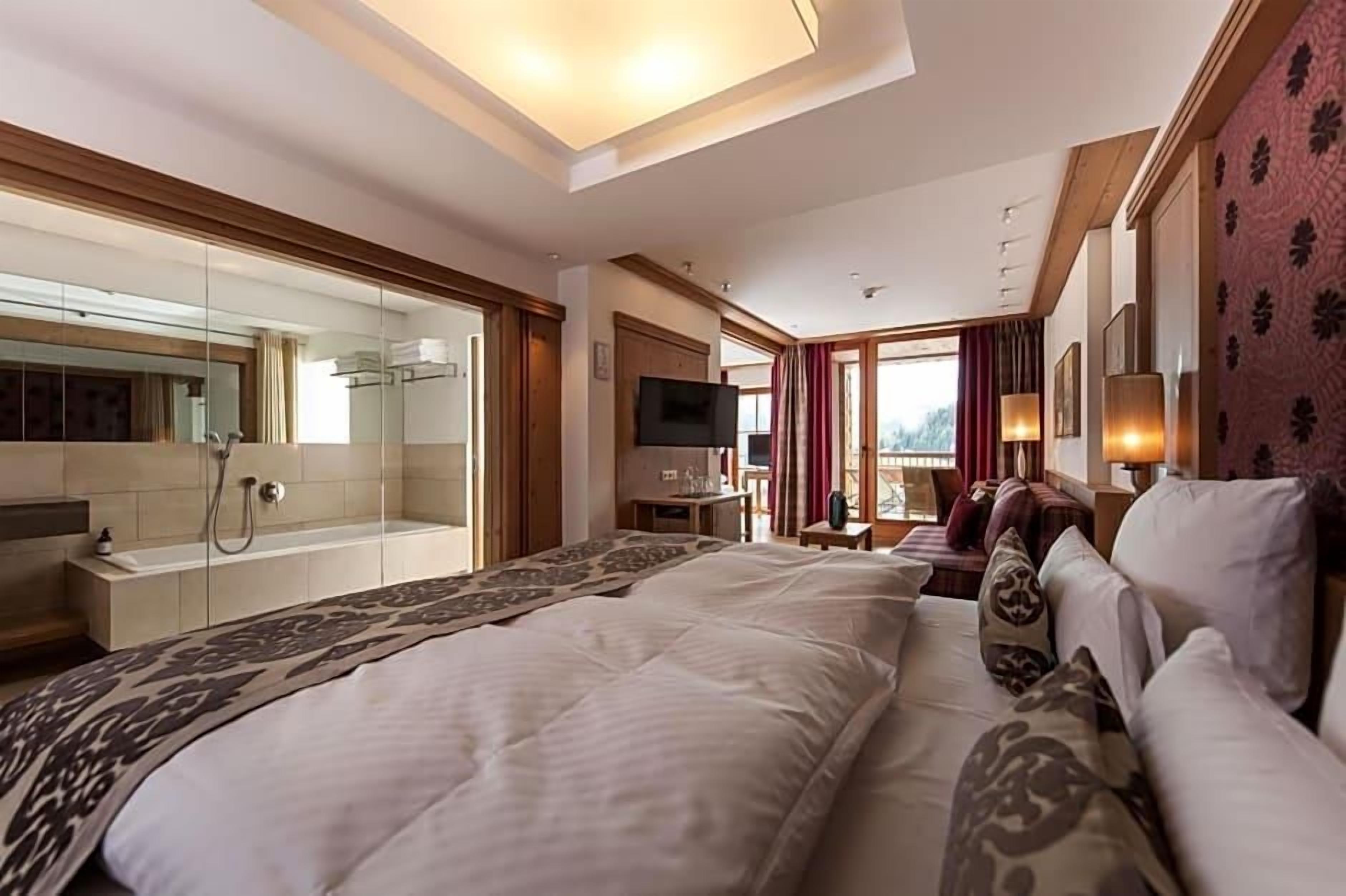 A hotel room with a large bed, a television, a desk, and a shower area.