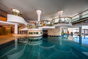 A multi-level indoor swimming pool with glass railings and a central water feature.