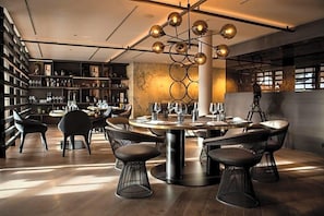 A modern dining area with a round table, black wireframe chairs, and a unique ceiling light fixture.