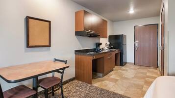 A compact kitchen with a dining table and chairs, a refrigerator, and wooden cabinets.