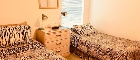 Un dormitorio con dos camas, una mesita de noche, un escritorio y una ventana con persianas.