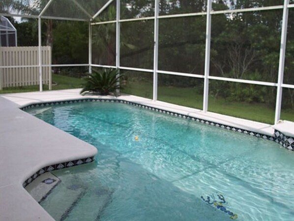 A rectangular pool with a white edge and a black and white tile pattern, surrounded by a white fence and a glass enclosure.