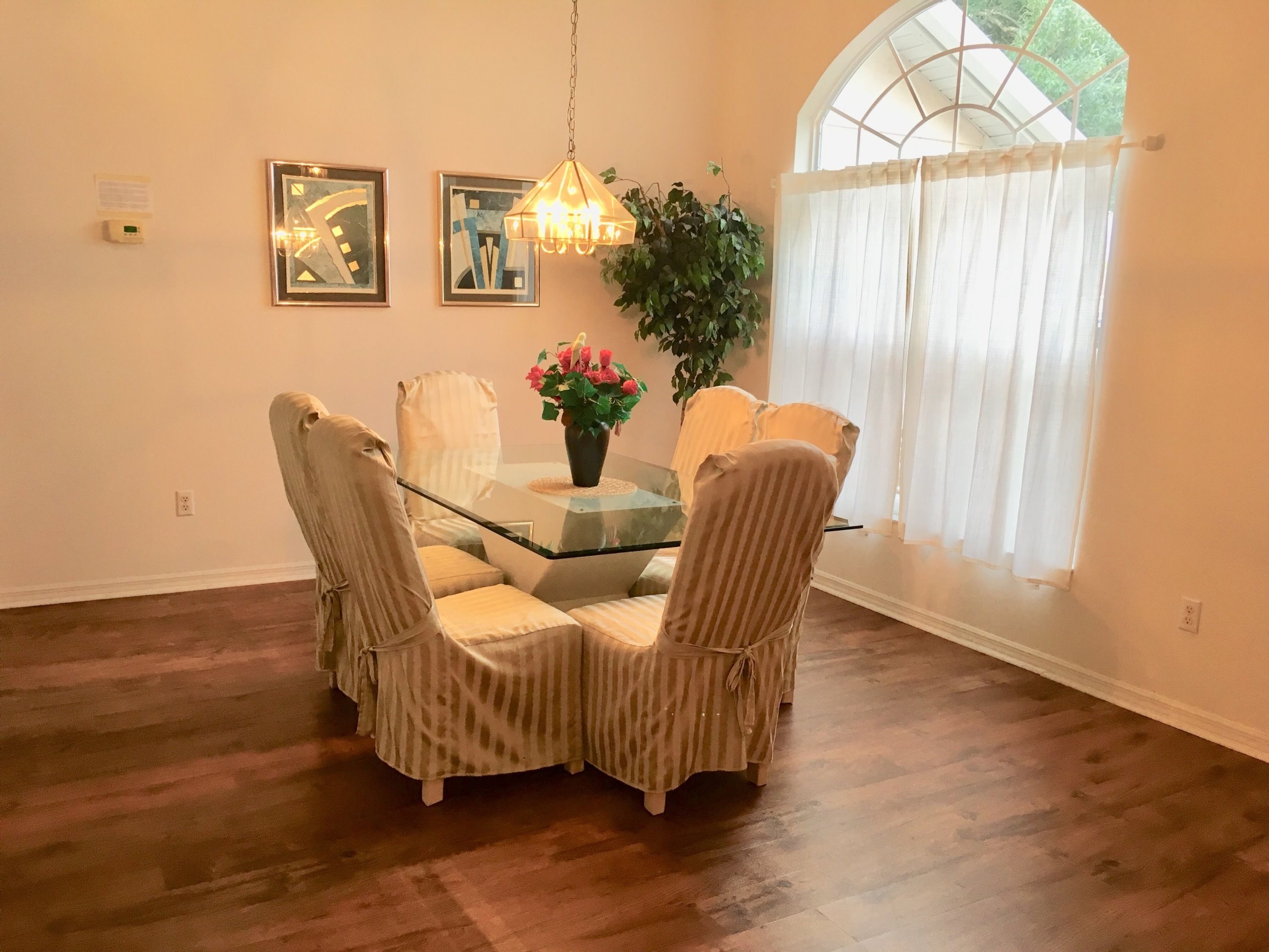 A dining area with a glass-top table, striped chairs, a potted plant, and a hanging light fixture.