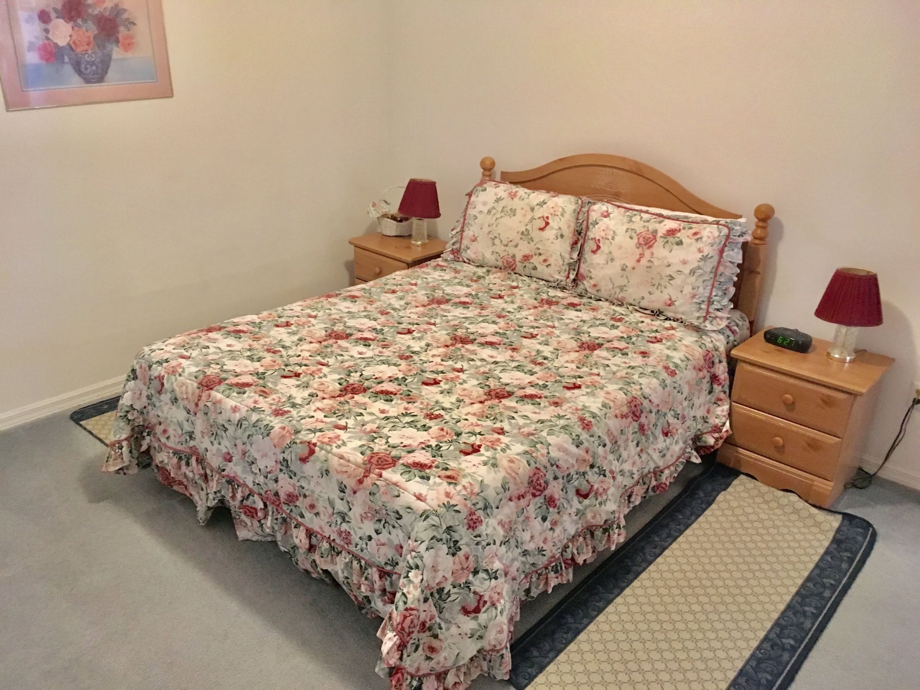 A bedroom with a floral bedspread, wooden headboard, two nightstands with lamps, and a small bedside table.