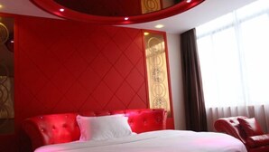Quarto de hotel com cabeceira estofada vermelha, cama com roupa de cama branca e poltrona de couro vermelha.