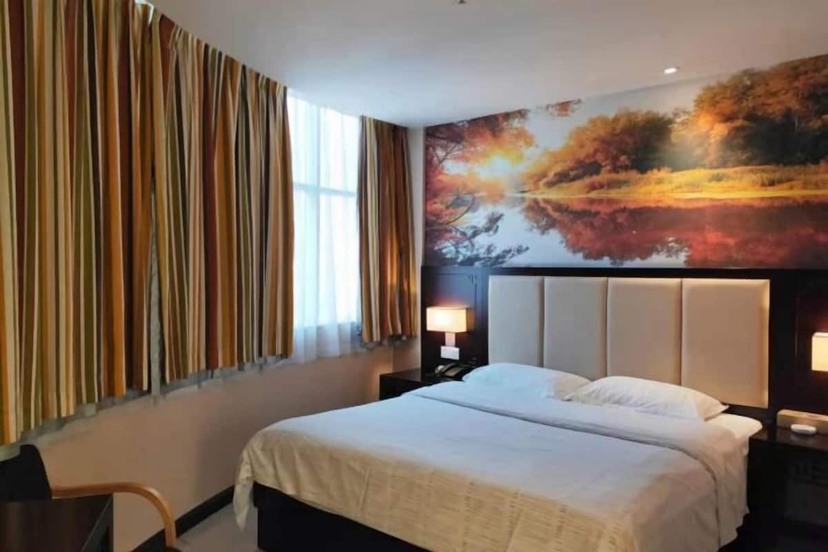 Una habitación de hotel con cama, mesita de noche, lámpara, silla y ventana con cortinas.